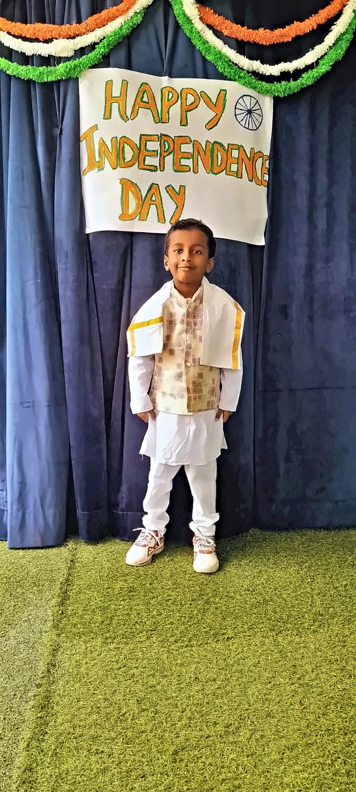 A boy in a white kurta and stole in front of the Independence Day banner