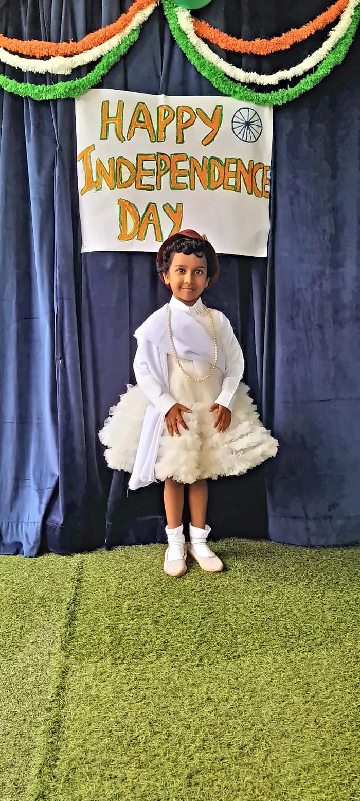 A girl dressed in white with a hat posing by the Independence Day banner
