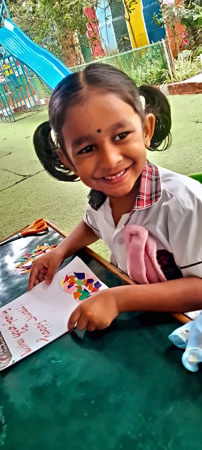 A smiling girl making a paper mosaic Diwali card at an outdoor table