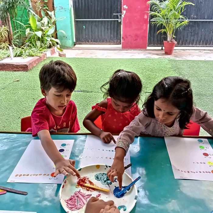 Three children dipping fingers in paint while filling in counting sheets