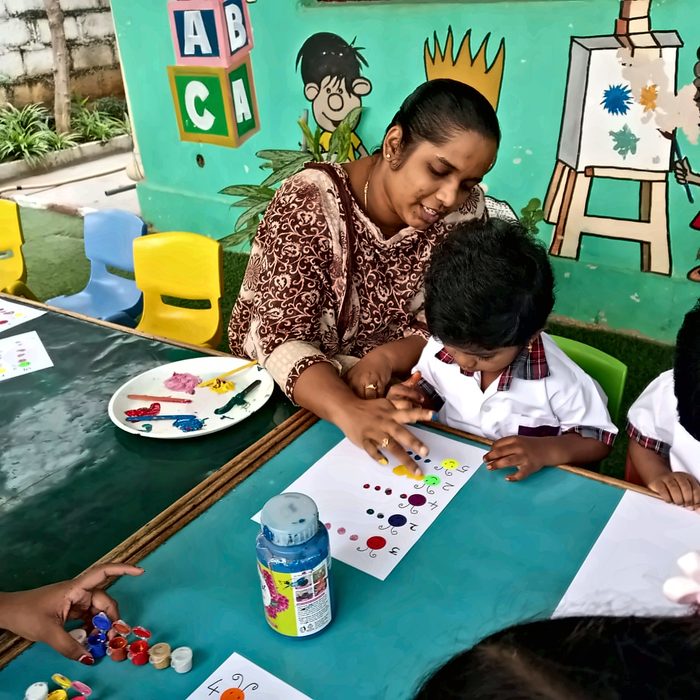 A teacher helping a young child place fingerprint dots on a worksheet