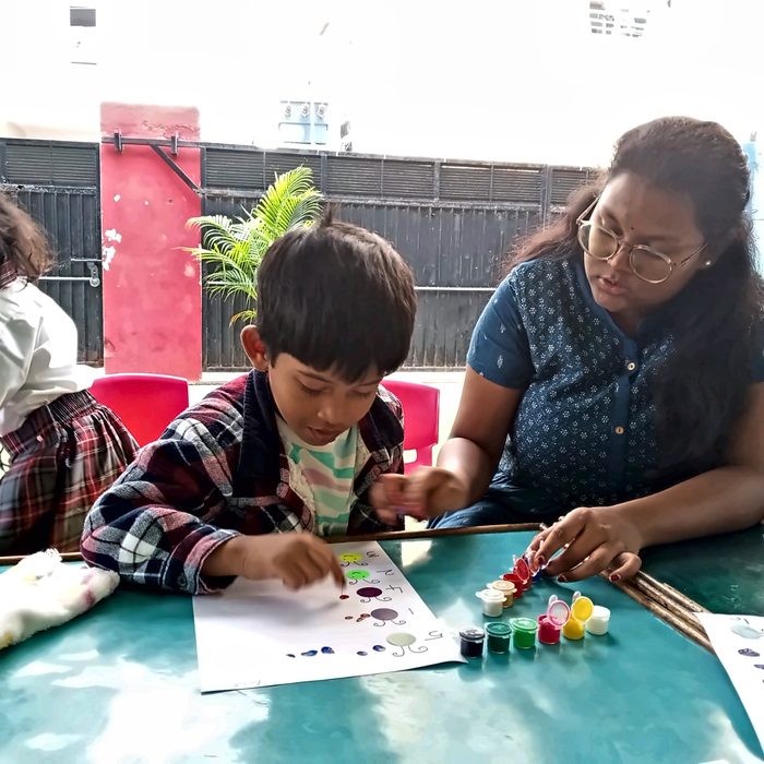A teacher guiding a boy through a fingerpaint counting activity