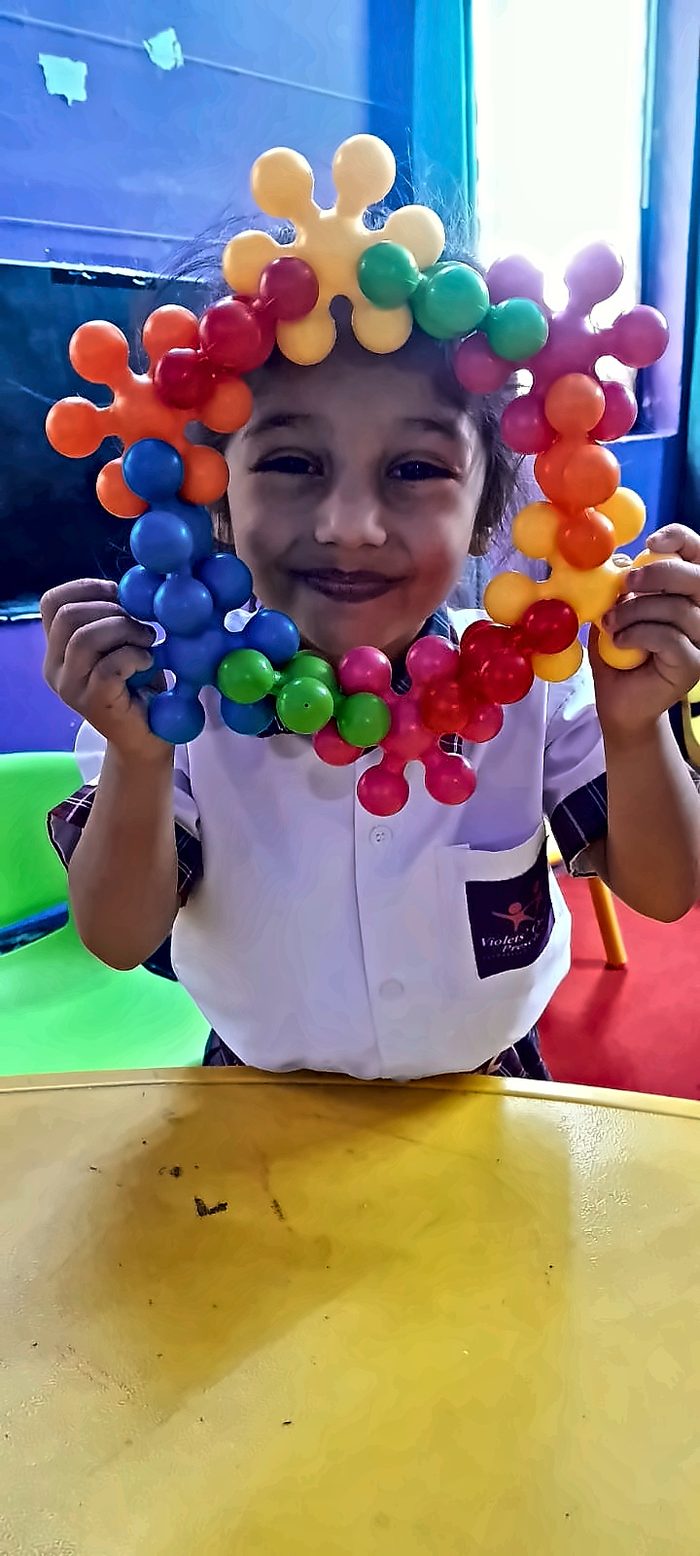 A smiling girl holding up a ring built from colourful connector toys