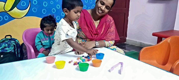 A teacher smiling as two children sort coloured pom-poms into cups