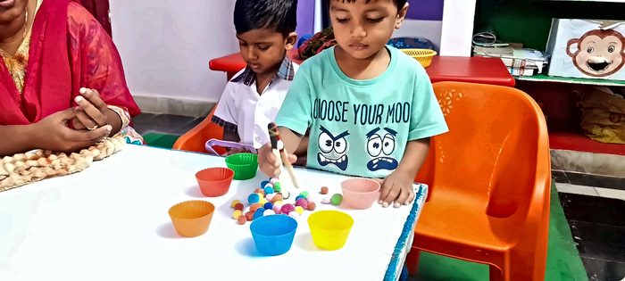 A boy using tongs to sort coloured pom-poms into cups